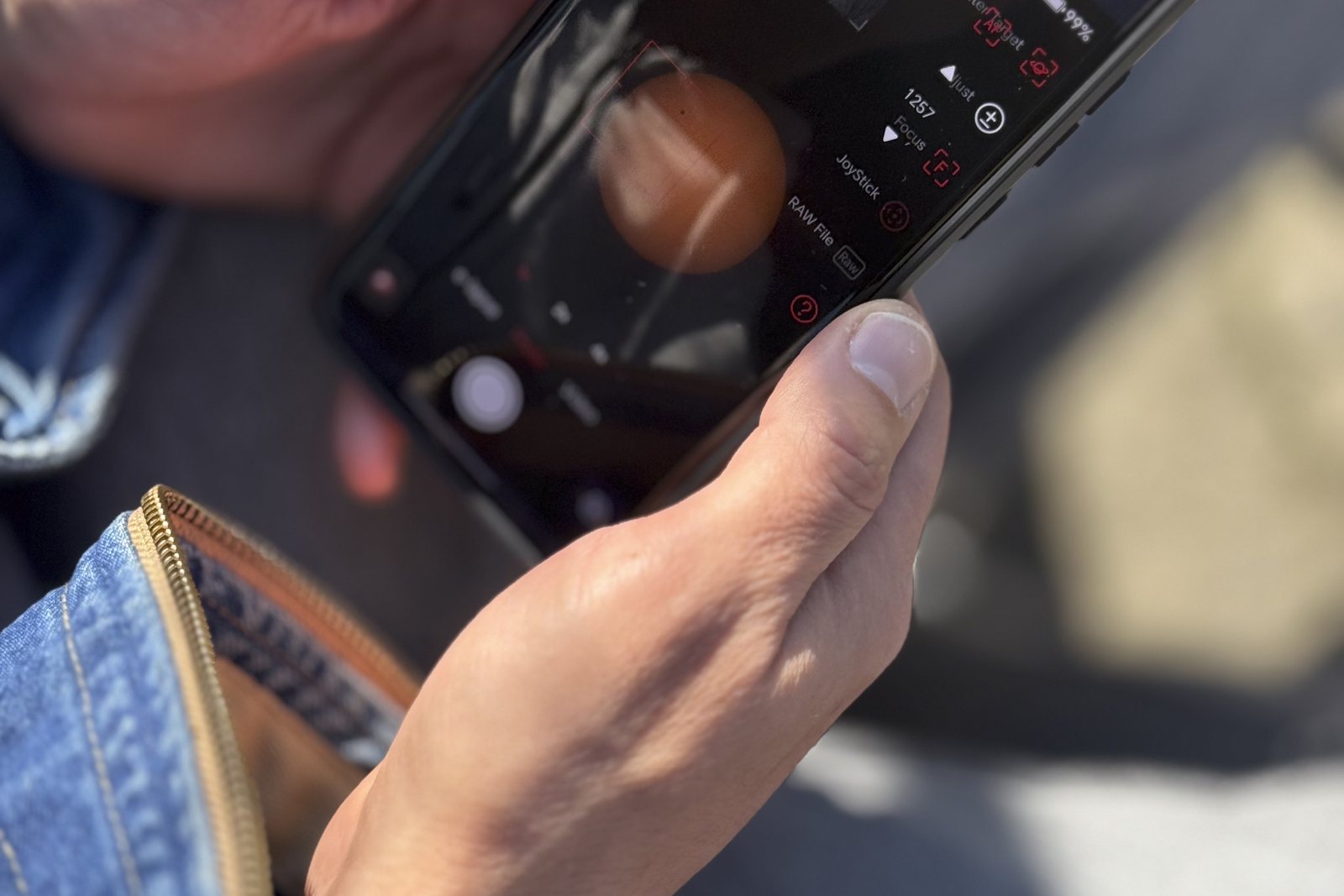 A person holding a smartphone outdoors on a sunny day
